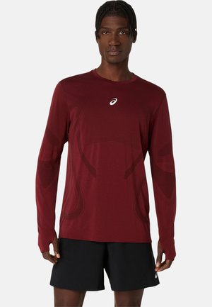 Langærmet atletisk skjorte i dyb rød med et subtilt design, rund hals og et logo på brystet. Stoffet ser glat og letvægtigt ud.