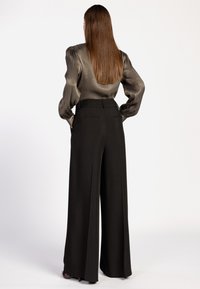 Zwarte wijde broek met zijzakken en een getailleerde pasvorm. Gecombineerd met een metallic top met lange mouwen en opbollende schouders.