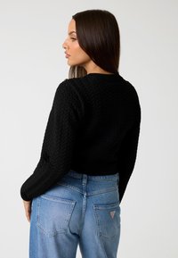 Maglione nero a trama goffrata con motivo a zigzag, dotato di scollo rotondo e polsini a costine, abbinato a jeans in denim blu chiaro a vita alta.