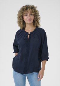 Navy blue linen blouse featuring a round neckline with a tie, three-quarter puff sleeves, and a decorative vertical lace trim.