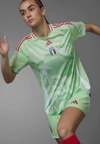 Zelena nogometna oprema z motivom listja, rdečimi poudarki in belim obrobnim. Vključuje značko "ITALIA" ter logotip Adidas na majici in kratkih hlačah.