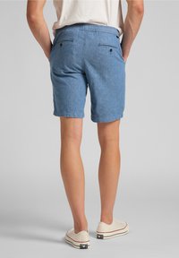 Pantalones cortos en denim azul con un ajuste relajado, dos bolsillos traseros con botones y un dobladillo vuelto, complementados con zapatillas blancas informales.