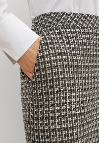 Pantalon en tweed à motif noir, blanc et rose. Il comporte des poches latérales et une taille ajustée. Le tissu texturé ajoute de la profondeur.