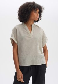 Blusa leggera a coste con scollo a V e maniche corte arrotolate in un colore neutro, abbinata a pantaloni neri larghi.
