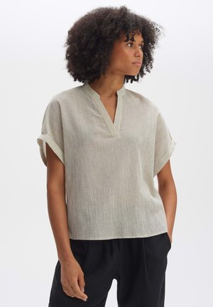 Lichte, geribbelde blouse met een V-hals en korte omgeslagen mouwen in een neutrale kleur, gecombineerd met losse zwarte broeken.