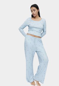 Lichtblauw pyjamaset met lange mouwen en elastische tailleband, met een geribbelde structuur en kleine zwarte hartpatronen.