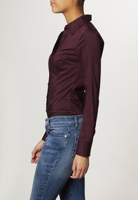 Camisa burdeos de manga larga con cuello, con un diseño ajustado, parte delantera abotonada y tejido suave y ligeramente brillante.