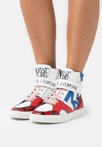 Vysoké sneakersy s kombinací červené, modré a bílé syntetické materiály, s texturovaným hadím vzorem a potištěnými tkaničkami.