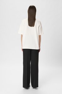 Tricou alb din bumbac, cu mâneci scurte, asortat cu pantaloni negri, cu talie înaltă și cu croială largă. Textură netedă, croială lejeră și fără modele vizibile.