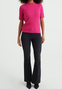 Kortärmad stickad tröja i ljusrosa, med ett strukturerat diamantmönster och ribbad halsringning, i kombination med åtsittande svarta utsvängda jeans.