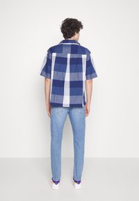 Kortärmad rutiga skjorta i marinblå och ljusblå nyanser, med avslappnad passform och mjukt bomullsmaterial, matchad med ljusblå jeans.