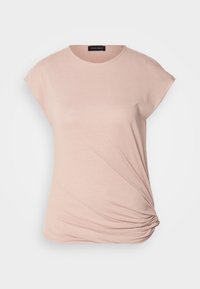 Top de manga corta rosa claro, hecho de una tela suave, con un escote redondo y un detalle de nudo drapeado en un lado para añadir textura.