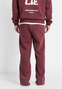 Bordeauxfarbener Hoodie mit Text auf dem Rücken, kombiniert mit passenden bordeauxfarbenen Jogginghosen. Baumwollmischung, lockerer Schnitt und gerippte Bündchen.