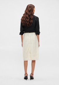 Camiseta preta curta com mangas enroladas, acompanhada de uma saia creme com bordados florais. O modelo usa sandálias de salto alto pretas.