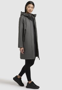 Grijze waterdichte parka met een capuchon, verstelbare trekkoorden, zijrits zakken en een rechte snit, gecombineerd met zwarte leggings en sneakers.
