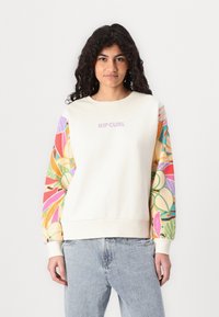 Sudadera crema con mangas de patrón tropical colorido. Presenta un cuello redondo y un logo "RIPCURL" en la parte frontal. Tejido de algodón suave.