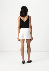 Svart, ermeløs topp med V-hals kombinert med hvite shorts. Shortsene har baklommer og en jevn tekstur.