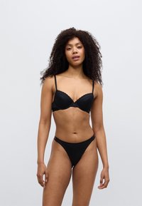 Σετ μαύρου εσωρούχου που περιλαμβάνει στηθόδεσμο με ενσωματωμένη ενίσχυση και δαντελένιο τελείωμα, με ρυθμιζόμενους ιμάντες, σε συνδυασμό με τανγκι επιλεγμένου σχεδίου. Λείο ύφασμα, μινιμαλιστικός σχεδιασμός.