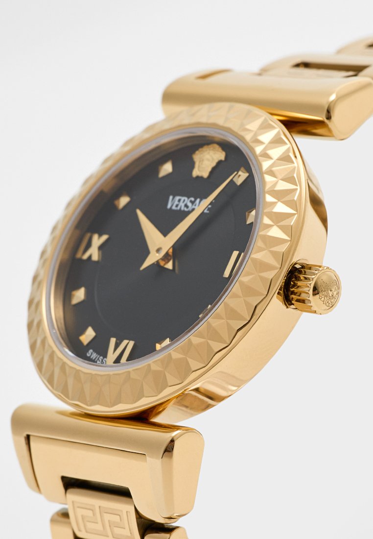 Gouden horloge met een geprofileerde lunette, zwarte wijzerplaat en gouden uurmarkeringen. Voorzien van een klapsluitingarmband en een logo op de wijzerplaat.