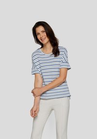 Striped knit top in blue and white, short sleeves, crew neckline, relaxed fit, featuring subtle texture and side vents. Paired with light pants.