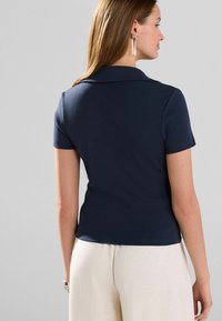 Marineblå polo t-shirt med korte ærmer, en flad krave, lavet af glat stof. Bæres med lyse, løst siddende bukser.