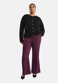 Cardigan en tricot noir avec un col blanc, fermeture à boutons, associé à un pantalon large violet foncé et des escarpins noirs à bout pointu.