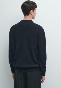 Granatowy sweter dzianinowy z okrągłym dekoltem, długimi rękawami i ściągaczami na mankietach. Miękka faktura i luźny fason, z prostym wzorem bez zdobień.