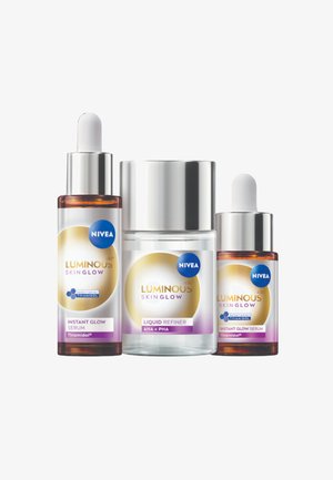 Drei NIVEA Hautpflegeprodukte: zwei Tropfflaschen aus bernsteinfarbenem Glas und ein transparentes Glas, alle mit weißen Verschlüssen und farbenfrohen Etiketten mit goldenen Akzenten.