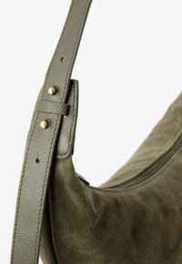 Sac à bandoulière en daim vert olive avec une finition texturée, doté d'une large sangle en cuir et d'accents en métal sur la sangle.