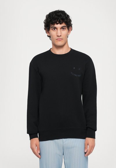 Black sweatshirt with long sleeves, crew neck, and a subtle logo on the left chest. Soft fabric with a relaxed fit. Paired with light striped pants.