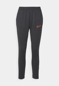 Pantalones deportivos negros con un diseño ajustado, cinturilla elástica y logo de Nike en color naranja en la cadera izquierda. Textura de tejido suave y elástico.
