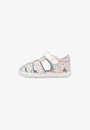 Sandalia blanca para niño pequeño con patrones multicolores de estrella, corazón, corona y peine, correa de velcro y suela blanca perforada.