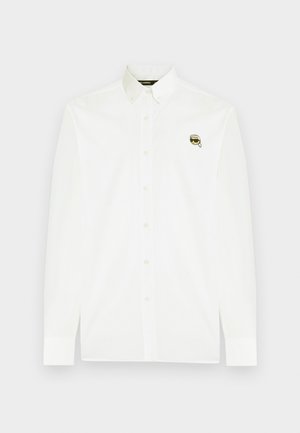 Bijela košulja od pamuka s klasičnim ovratnikom, dugim rukavima i malim crno-zlatnim logotipom na prsima.