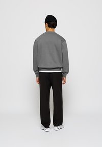 Gray sweatshirt with dropped shoulders, ribbed cuffs, and hem, paired with black pants and white sneakers on a plain background.
