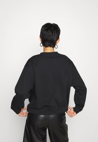 Zwarte sweatshirt met verlaagde schouders en ribgebreide zoom. Gecombineerd met zwarte imitatieleren broek. Eenvoudig ontwerp, geen zichtbare patronen of accenten.