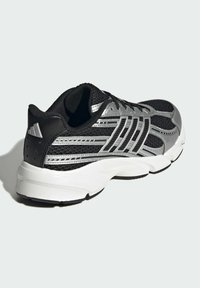 Čierna a strieborná atletická obuv s mesh vrchnou časťou, polstrovanou podrážkou a výrazným trojprúžkovým dizajnom na boku pre lepšiu priedušnosť.