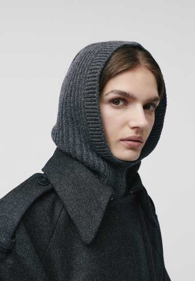 Cappotto di lana grigio scuro con cappuccio in maglia grigia a coste. Presenta un ampio colletto, dettagli con bottoni sulla spalla e una texture liscia.