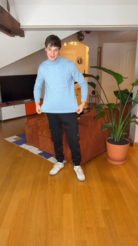 Lys blå langermet skjorte i bomullsblanding, avslappet passform. Svarte cargobukser med smal fasong. Hvite joggesko med glatt tekstur. Innendørs miljø med planter.