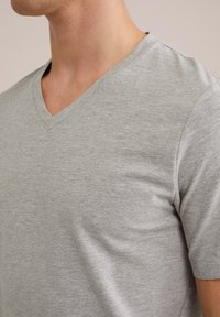 Camiseta de cuello en V de color gris claro, hecha de algodón suave y liso. Presenta un ajuste casual con mangas cortas y un acabado sutil y texturizado.