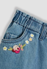 Blaue Jeanshose mit elastischem Bund und gestickten rosa, weißen und gelben Blumen in der Nähe der Vordertasche.