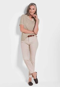 Beige V-Ausschnitt Kurzarmtop, kombiniert mit hellbraunen Hosen und dunklen Slippern. Hat eine lockere Passform und eine dezente Textur. Brauner Gürtel setzt Akzente.