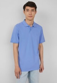 Jasnoniebieska koszulka polo z teksturowanej tkaniny, z klasycznym kołnierzykiem, dwiema guzikami przy szyi oraz krótkimi rękawami. Umieszczona na jednolitym tle.