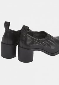 Chaussures en cuir noir avec un bout arrondi, un design bas et un talon épais. Présente des plis subtils et une languette à l'arrière.