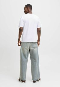 Camiseta blanca de manga corta combinada con unos vaqueros de pierna ancha de color azul claro. El conjunto presenta un ajuste relajado y un diseño minimalista sin patrones visibles.
