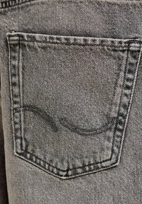 Zadné vrecko sivých džínsov z denimovej tkaniny s čiernym zakriveným prešitím na štruktúrovanej látke.