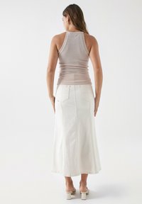 Top sin mangas ajustado color rosa claro con bordes en forma de ondas, combinado con una falda maxi de mezclilla blanca que cuenta con bolsillos traseros y costuras visibles.