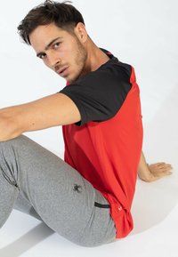 Ropa de deporte para hombres: camisa roja de manga corta con acentos negros, tela texturizada, combinada con pantalones ajustados grises que presentan un logo de araña negro.