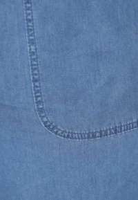 Denim-fabrikk i lys blå med en glatt tekstur. Har en buet lomme med detaljert søm langs kantene.
