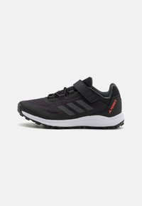 Baskets de sport noires avec une tige en maille, accents gris, bande Velcro et semelle texturée. Présente trois bandes gris foncé et un branding rouge.