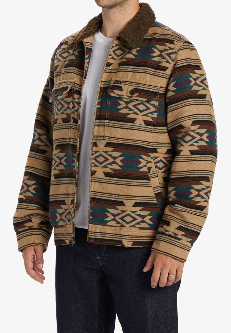 Tan patterned jacket featuring geometric designs in brown and teal, with a faux fur collar, two chest pockets, and a relaxed fit.